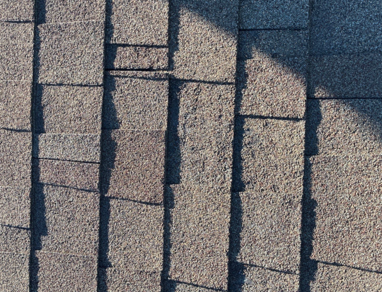 before_05 - Driftwood Builders Roofing Close-up of textured asphalt roof shingles in gray-brown tones with shadows emphasizing vertical seams.