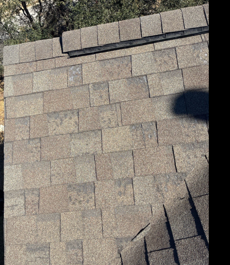 before_04 - Driftwood Builders Roofing Aerial view of a gray asphalt shingle roof with a metal vent along the top edge and shadows across the surface.