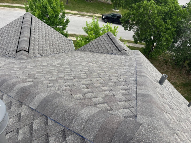 after_01 - Driftwood Builders Roofing Bird's-eye view of a gray shingle roof with multiple slopes, with a street and green trees visible in the background.