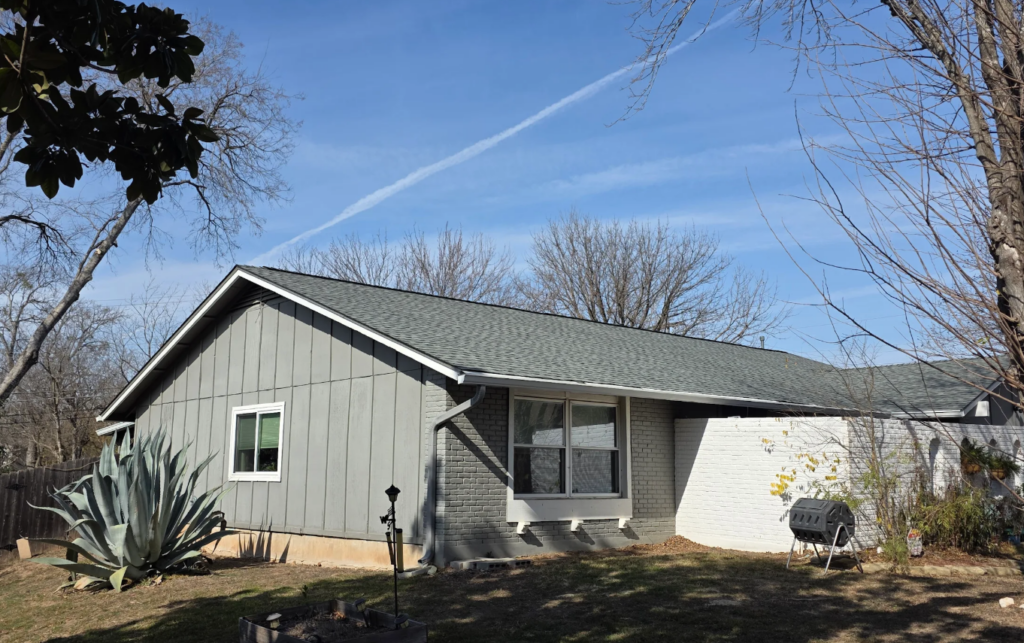 Single-story gray house with a white brick extension, a large agave plant in the yard, and a clear blue sky.