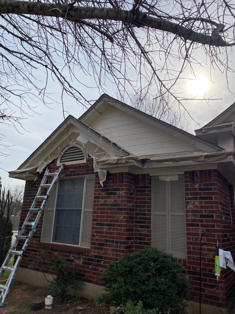 Leander_During_1 1 - Driftwood Builders Roofing Ladder propped against a brick house with plastic sheeting along the eaves for exterior maintenance.