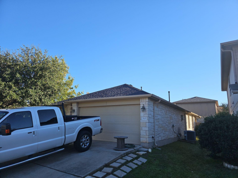 after_03_front_truck - Driftwood Builders Roofing White pickup truck parked in a suburban driveway in front of a stone-faced garage, under a clear blue sky.