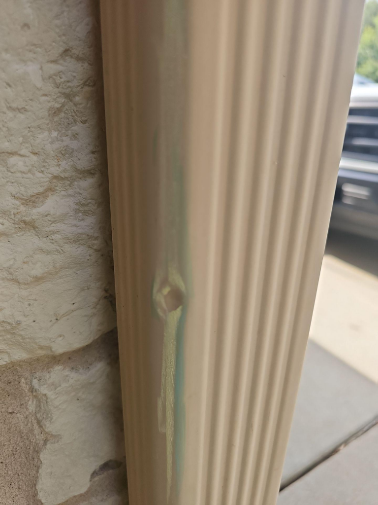 before_01_hail_damage_gutter - Driftwood Builders Roofing Close-up of a fluted beige pillar beside a rough stucco wall with a faint green vertical stain on the column edge.