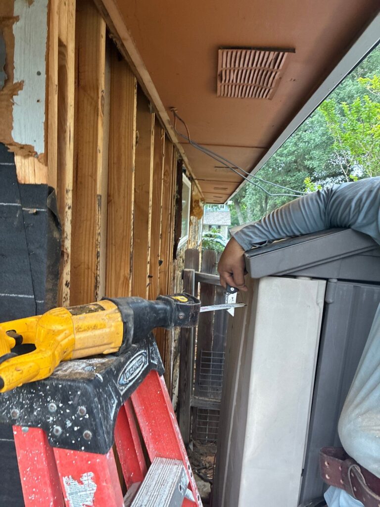 Narrow exterior wall renovation: exposed studs, wiring, and a yellow cordless drill resting on a red ladder beside a gray storage container.