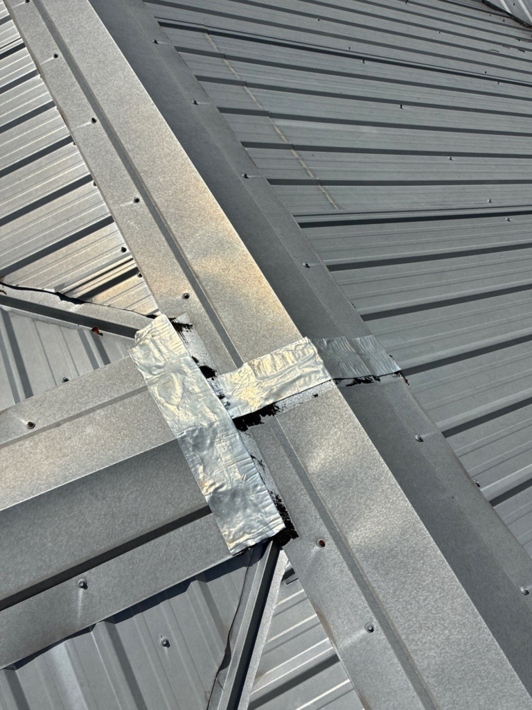Close-up of galvanized metal roof framing with intersecting beams and taped flashing strips.