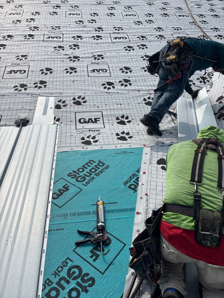 Wimberley_During_1 - Driftwood Builders Roofing Worker on a roof installing GAF TigerPaw underlayment with pawprint logos and StormGuard blue membrane visible; tools and backpack strapped to the worker.