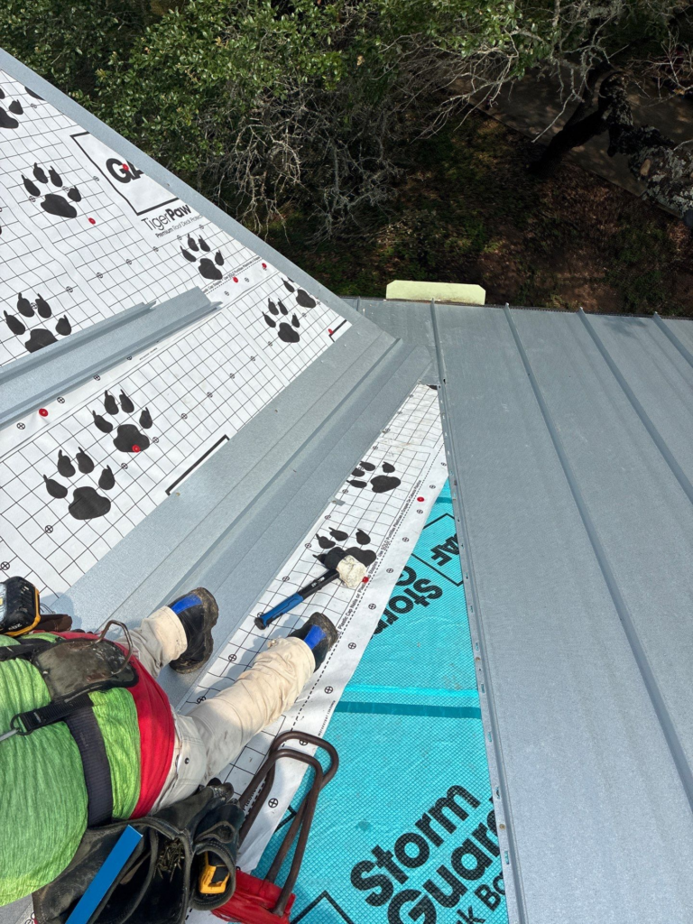 Wimberley_During_3 - Driftwood Builders Roofing Roof worker laying metal panels over white underlayment with paw print pattern, safety gear visible on the slope. Mush excitement?