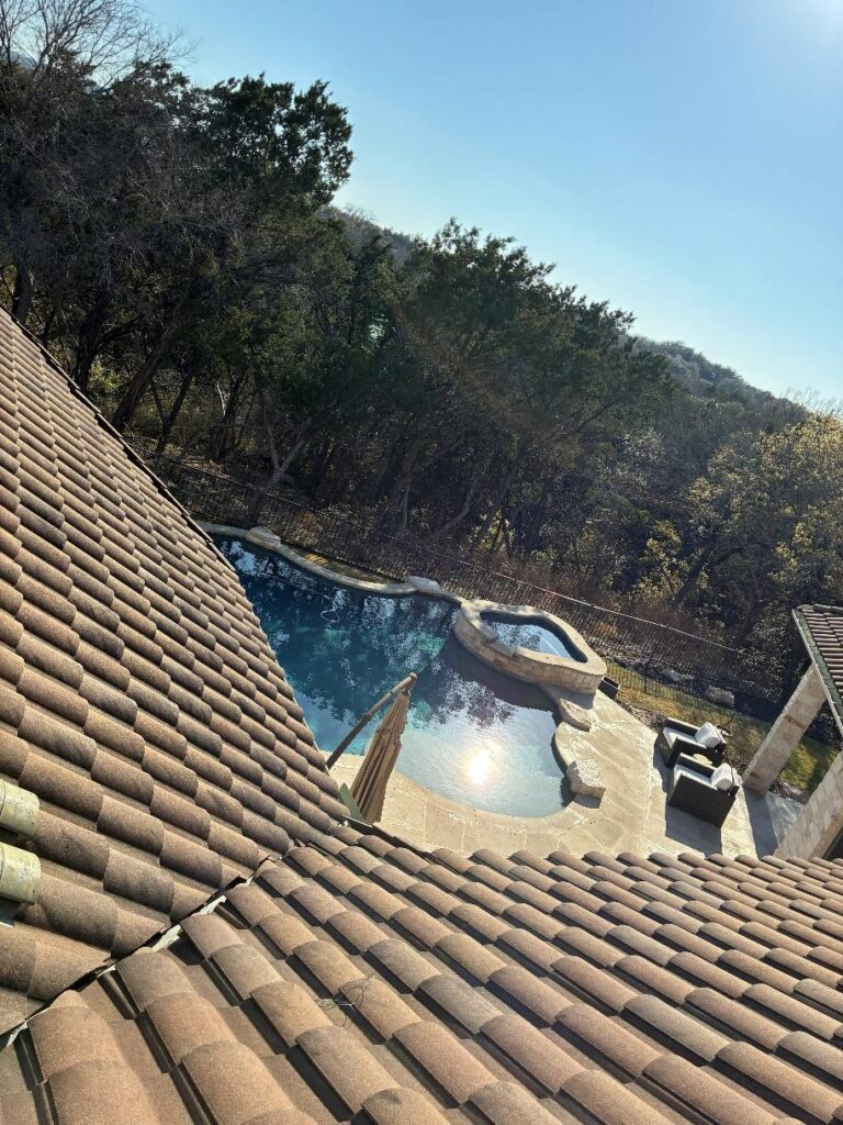 after_1 - Driftwood Builders Roofing Pool with curved spa, stone deck, and wicker seating—view from a tiled roofed patio on a sunny day.