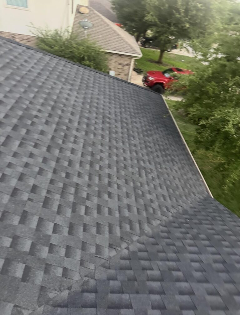 image15 - Driftwood Builders Roofing Overhead view of a gray shingled roof with a red pickup truck parked in a driveway and trees in the background.