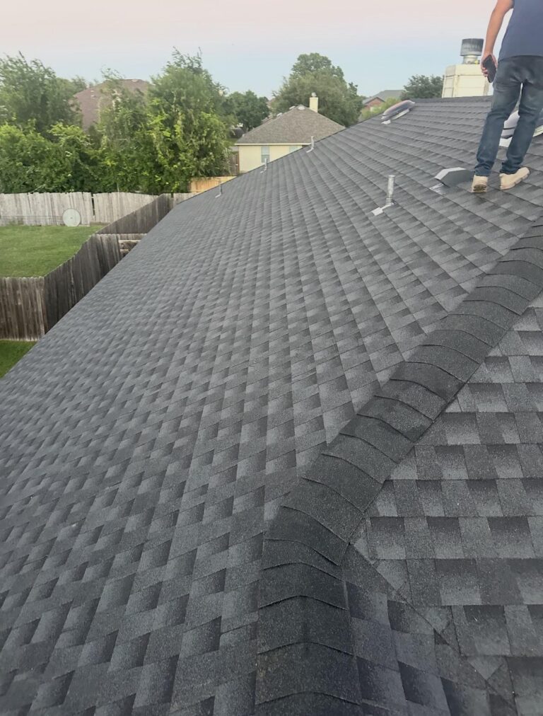 image13 - Driftwood Builders Roofing Person standing on a dark gray shingled roof with a tool in hand, performing maintenance or inspection against a suburban backyard backdrop.