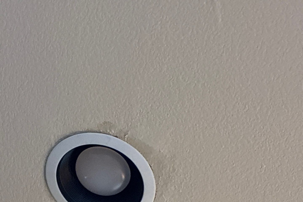 Round recessed ceiling light with white trim and dark interior on a textured beige ceiling.