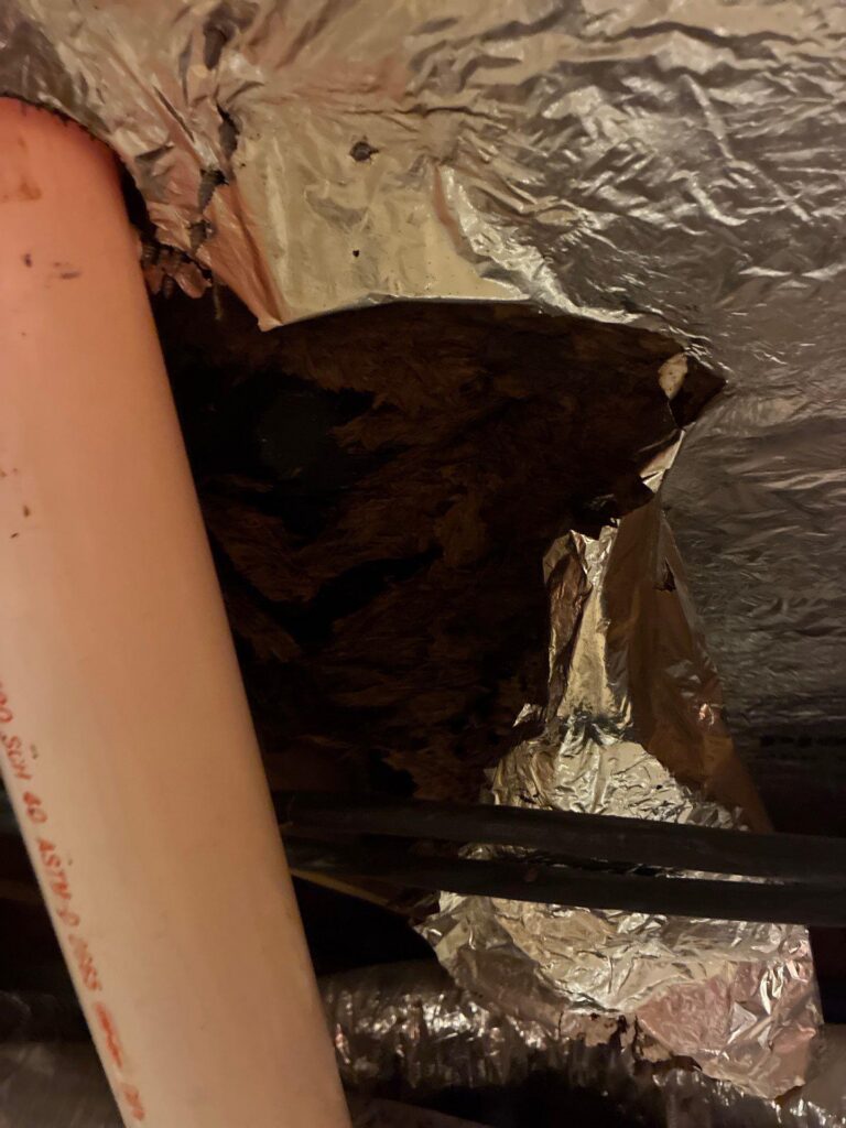 White PVC pipe running beside crumpled foil insulation in a dark attic or storage space.