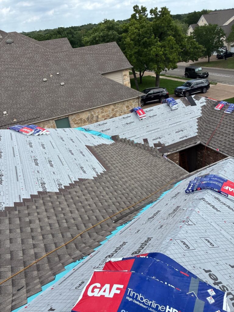 Rooftop under construction with brown shingles partially installed and GAF underlayment visible.