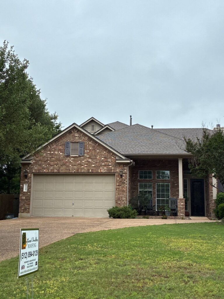 Brick suburban house with attached two-car garage, front porch, and a lawn sign for a roofing company in the yard, cloudy sky above