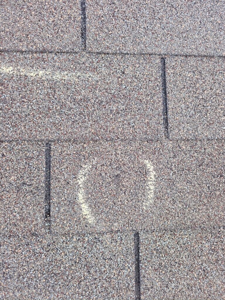 Close-up of brown asphalt roof shingles with a vertical seam and gritty granule texture.