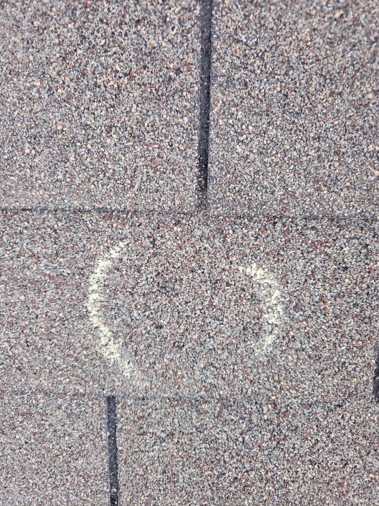 Close-up of rough asphalt surface with a vertical crack and faint yellow chalk markings forming a V shape at the bottom.