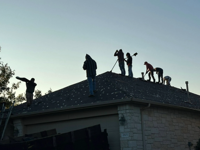 Several workers on a sloped residential roof, some with tools, during daytime construction on a suburban home