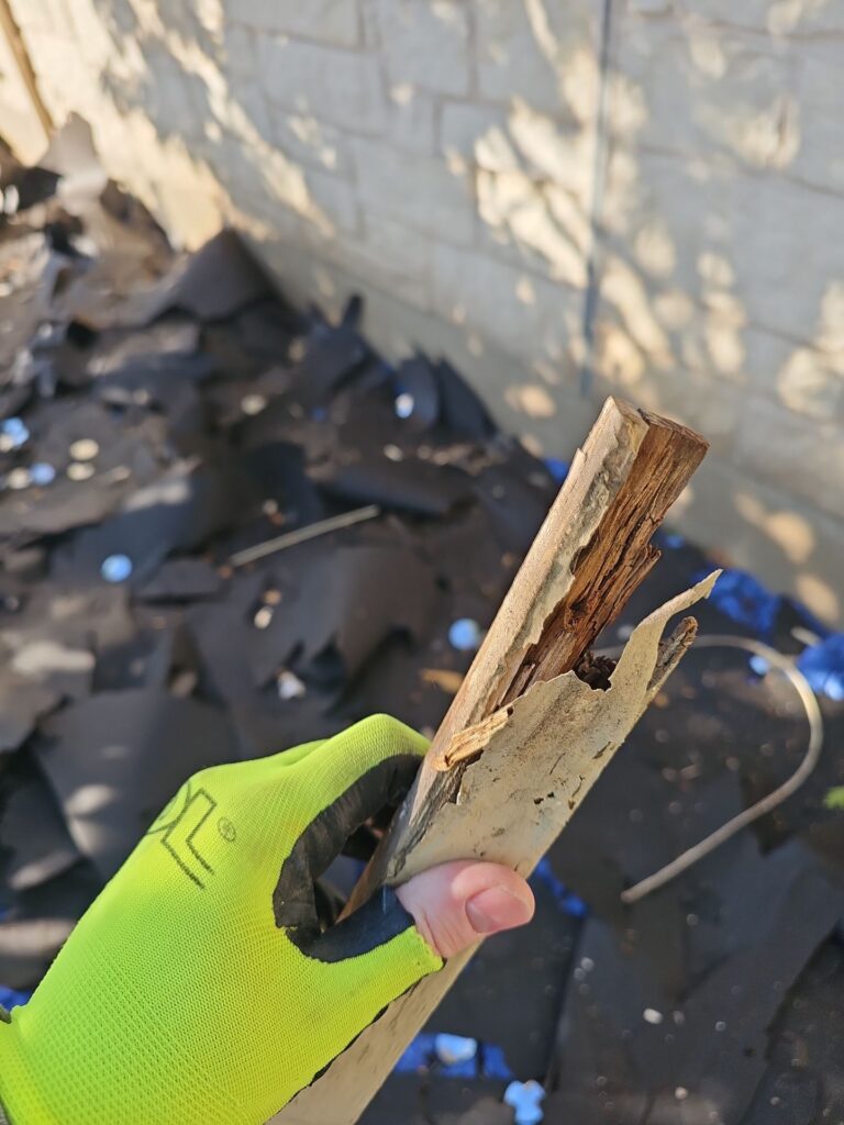 Person's gloved hand holds a jagged, weathered wooden splinter amid construction debris and rubble.