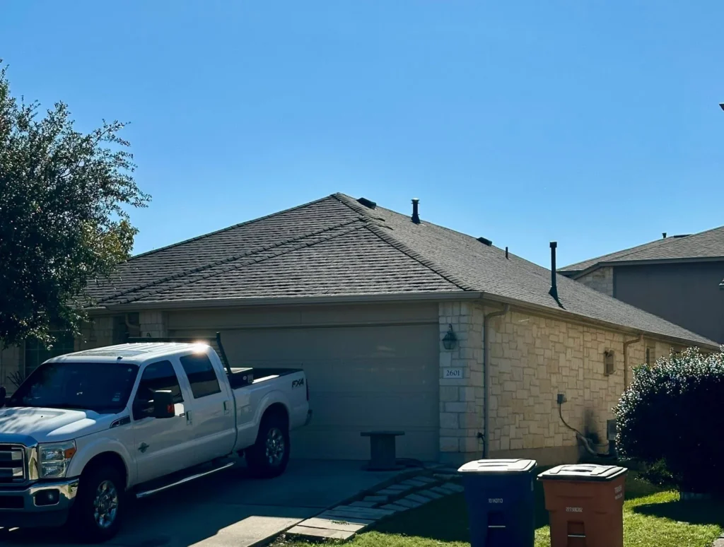 Front of a beige brick house with a pitched roof, a white pickup truck in the driveway, and blue sky above.
