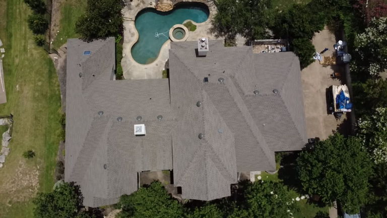 Aerial view of a large gray-roofed house with a kidney-shaped pool in the backyard.