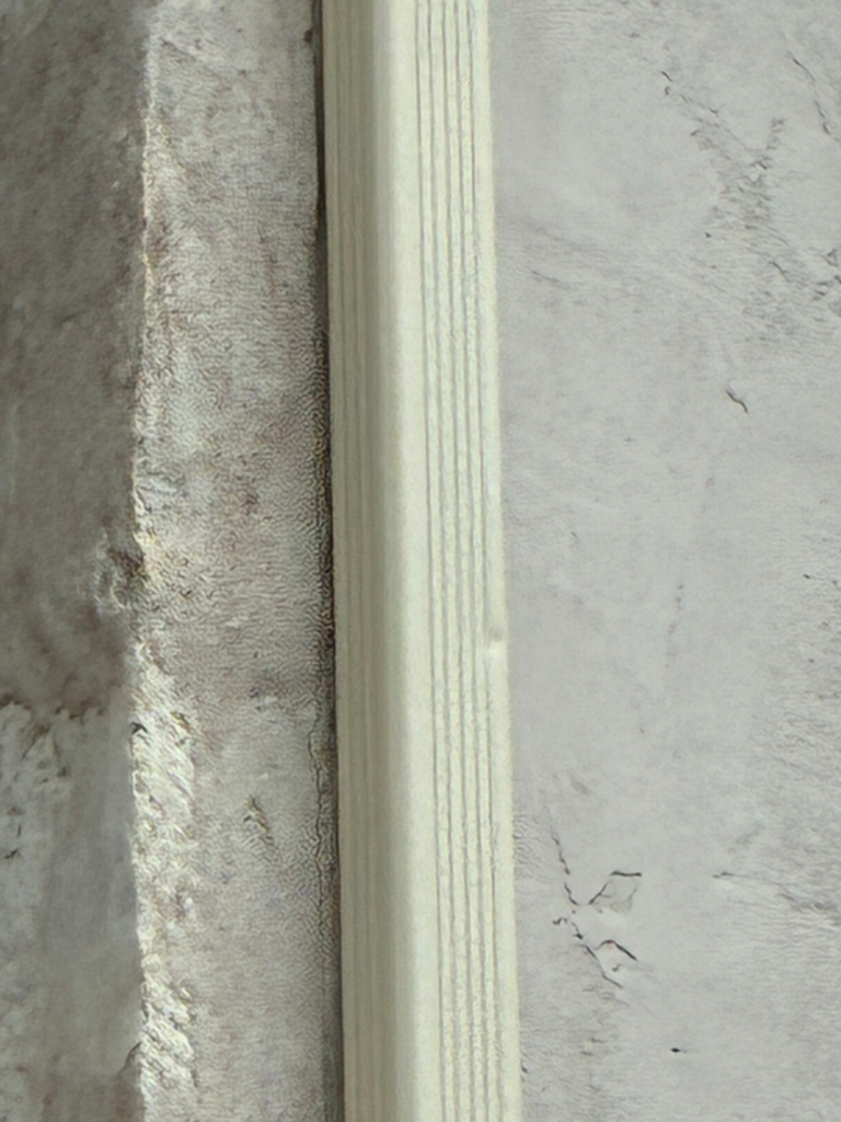 Close-up of a white grooved door trim between a rough textured wall on the left and a smooth, pale wall on the right.