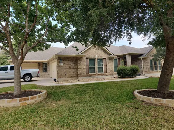 Brick single-story house with a driveway, a pickup truck, and a landscaped front yard framed by large trees.