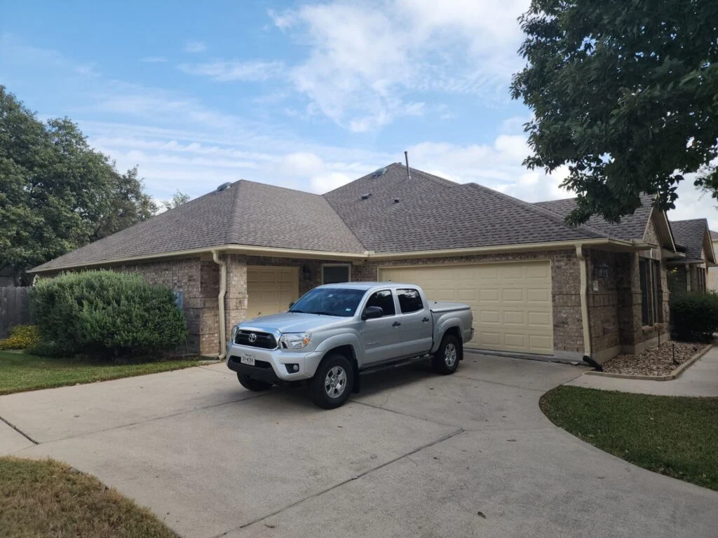 Silver Toyota pickup parked in front of a beige two-car garage on a suburban street.