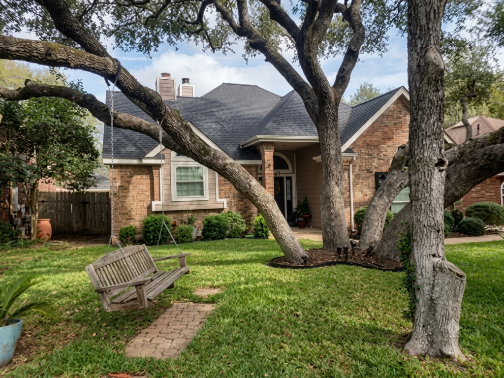 Brick suburban house with a covered front porch, large tree and wooden swing in the yard; green lawn and shrubs line the walkway to the door.