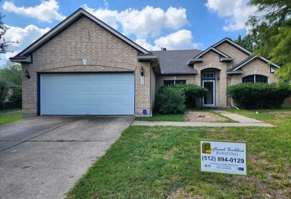 Brick single-family home with a two-car garage, a manicured front yard, and a roofing contractor sign in the yard.