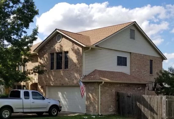 Two-story brick suburban house with an attached garage, a white pickup truck in the driveway, and an American flag near the entrance.