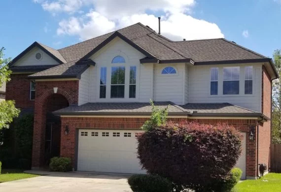 Two-story suburban house with brick and white siding, arched windows, and a two-car garage with a manicured front yard.