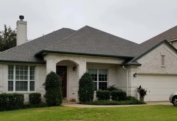 Front view of a single-story suburban house with an arched porch, two tall shrubs flanking the entrance, and a two-car garage; well-kept lawn in front.