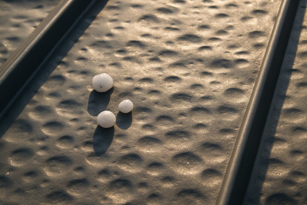 Three small white hailstones resting on a textured metal surface near a rail, casting long shadows in warm light.