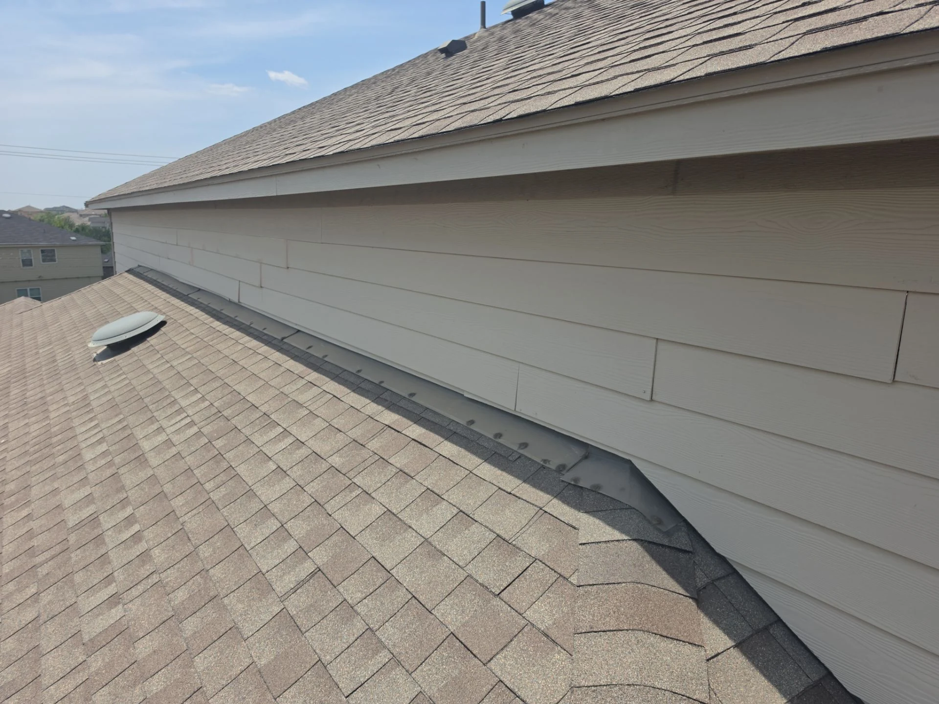 Continuous metal flashing along a roof-to-wall joint where fiber cement siding meets a lower roof slope on a Driftwood project.