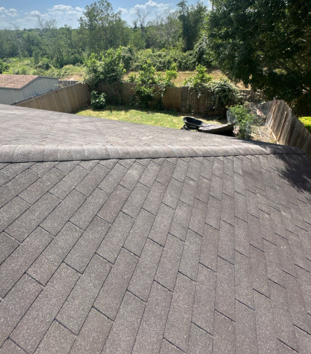 View from a sloped shingle roof looking toward a fenced backyard with a wheelbarrow and trees behind it.