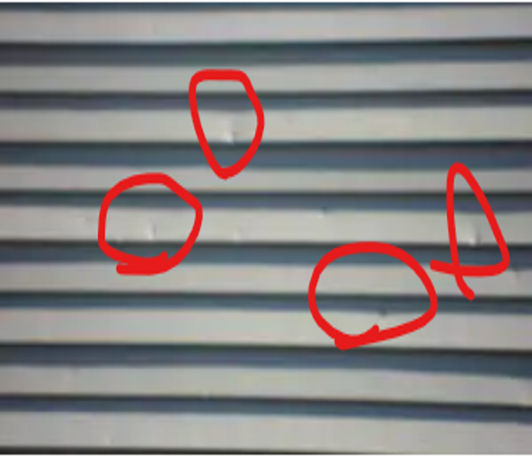 Gray corrugated metal siding with four red circles highlighting dents or damage areas? on the panels