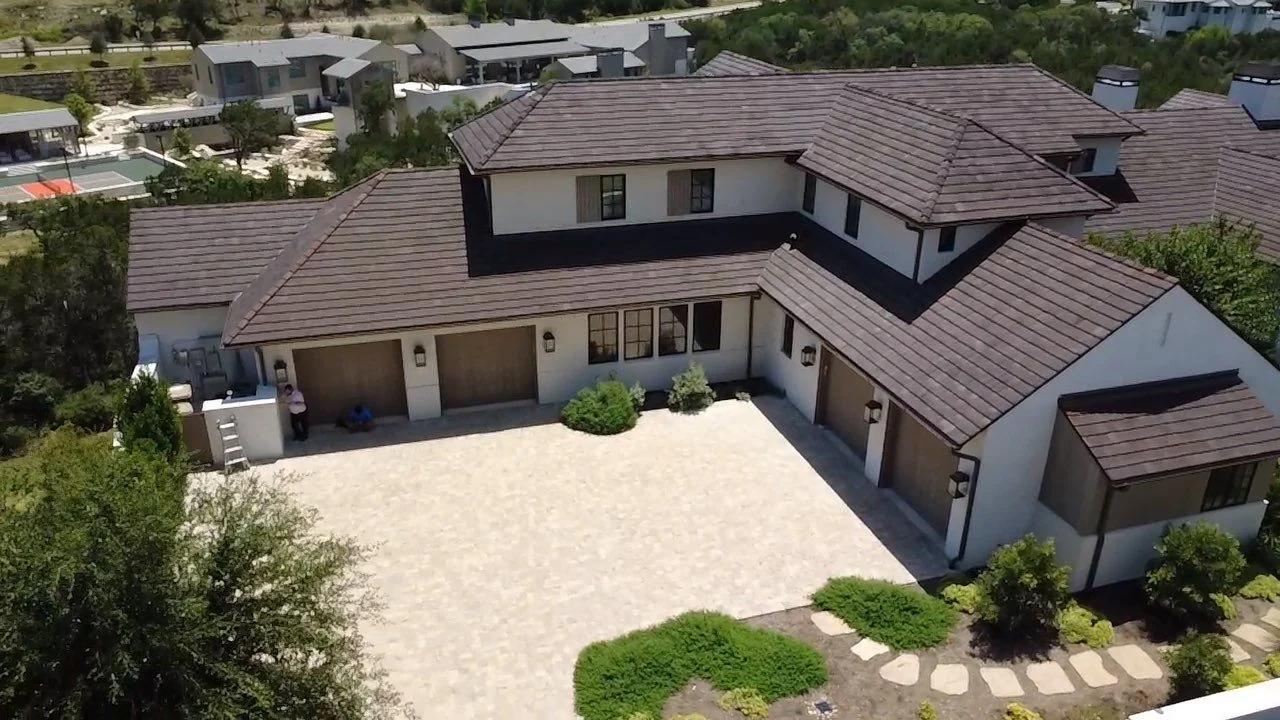 down-net_http20260831-208-g3ex2o - Driftwood Builders Roofing - Driftwood Builders Roofing A large two-story suburban home with multiple brown garage doors, tan tiled roof, and a light stone-paved driveway, viewed from above. Landscaping lines the front yard.