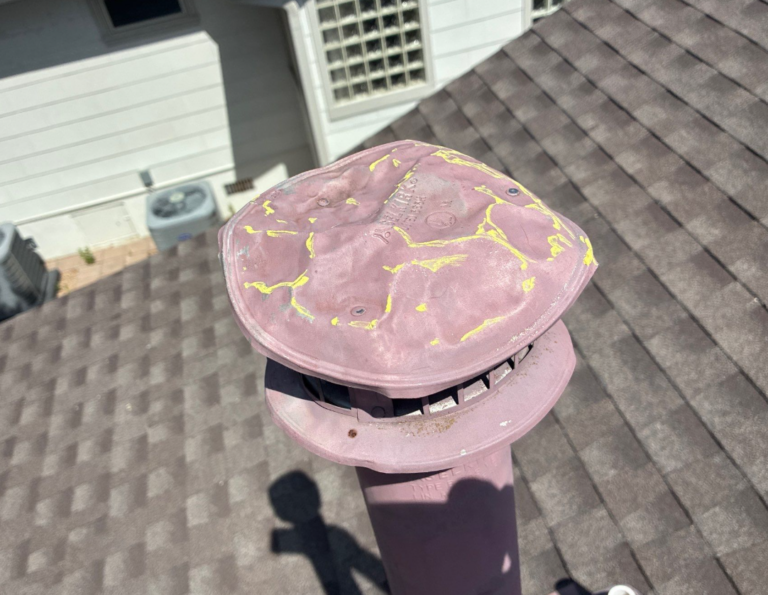 Close-up of a pink roof vent cap with peeling yellow paint on a sloped shingled roof (outdoor utility vent).