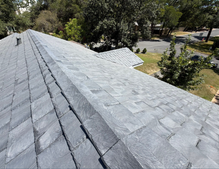 Aerial view of a gray slate roof with overlapping shingles on a suburban house, with trees and a street in the background.
