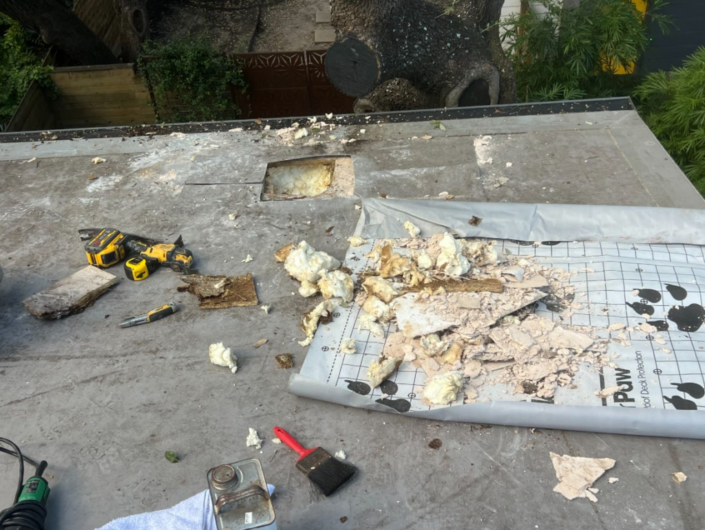 Rooftop renovation scene with torn insulation, debris, and scattered tools like a drill and brush.