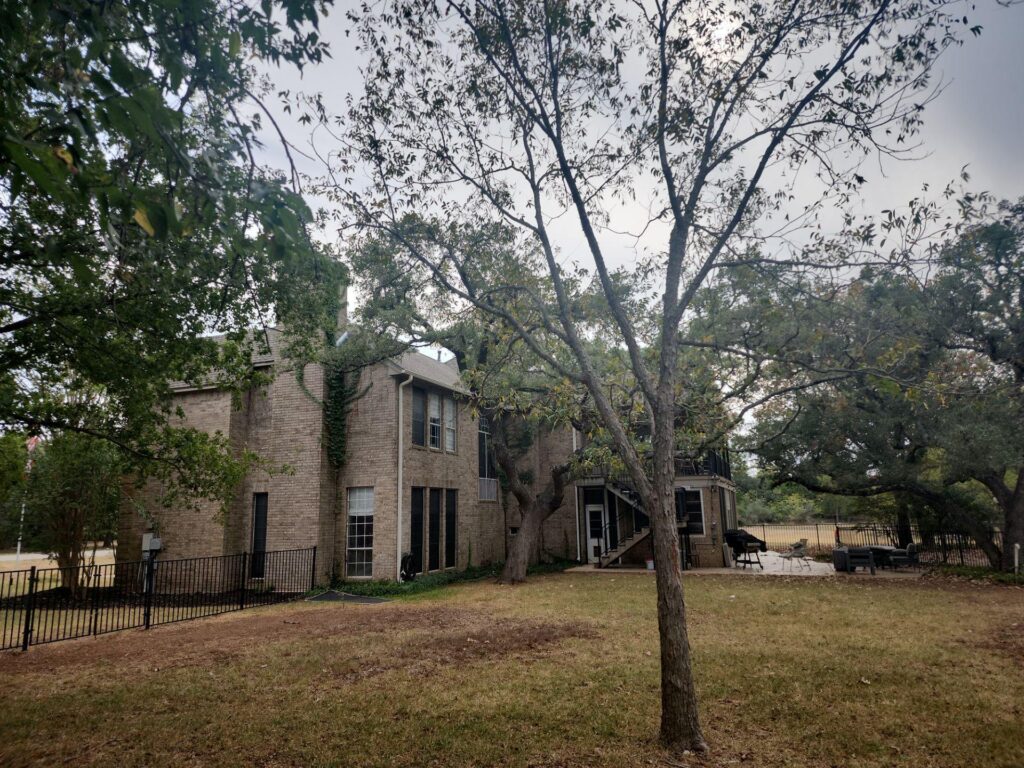 Brick two-story apartment building visible in a tree-filled yard with a metal fence along the edge.