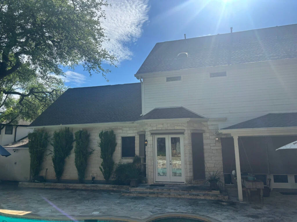 Sunny day view of a two-story house with a stone entry and pool in the foreground.