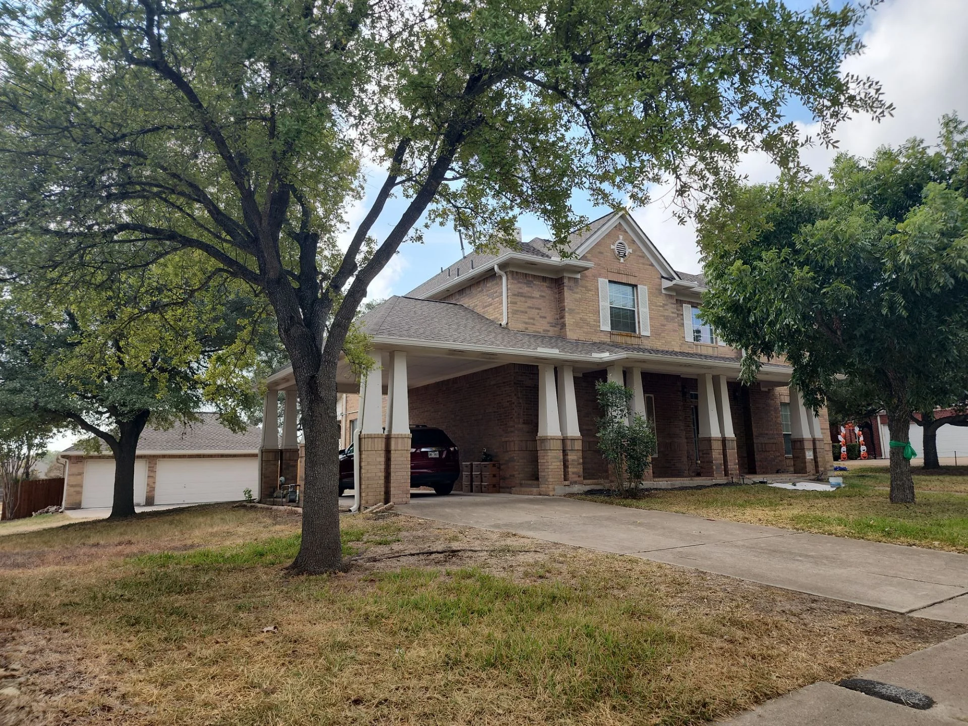 Two-story brick house with a covered front porch and white columns, a large tree dominates the yard, and a car is parked in the driveway.
