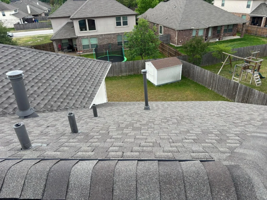 View from a sloped shingled roof overlooking neighboring backyards, with a trampoline, wooden playset, shed, and fenced yards.