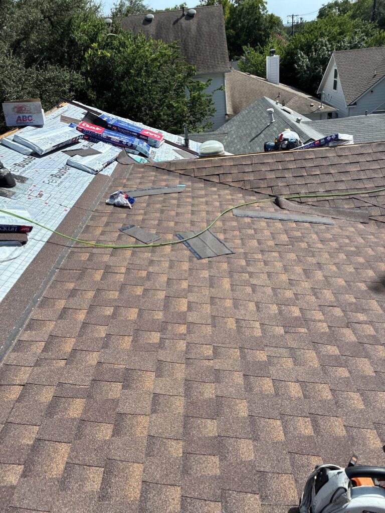 Rooftop under renovation with scattered tools, bundles of roofing underlayment, and exposed shingles for a residential re-roof project