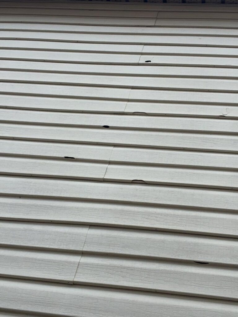 Hail punctures scattered across white vinyl siding lap boards