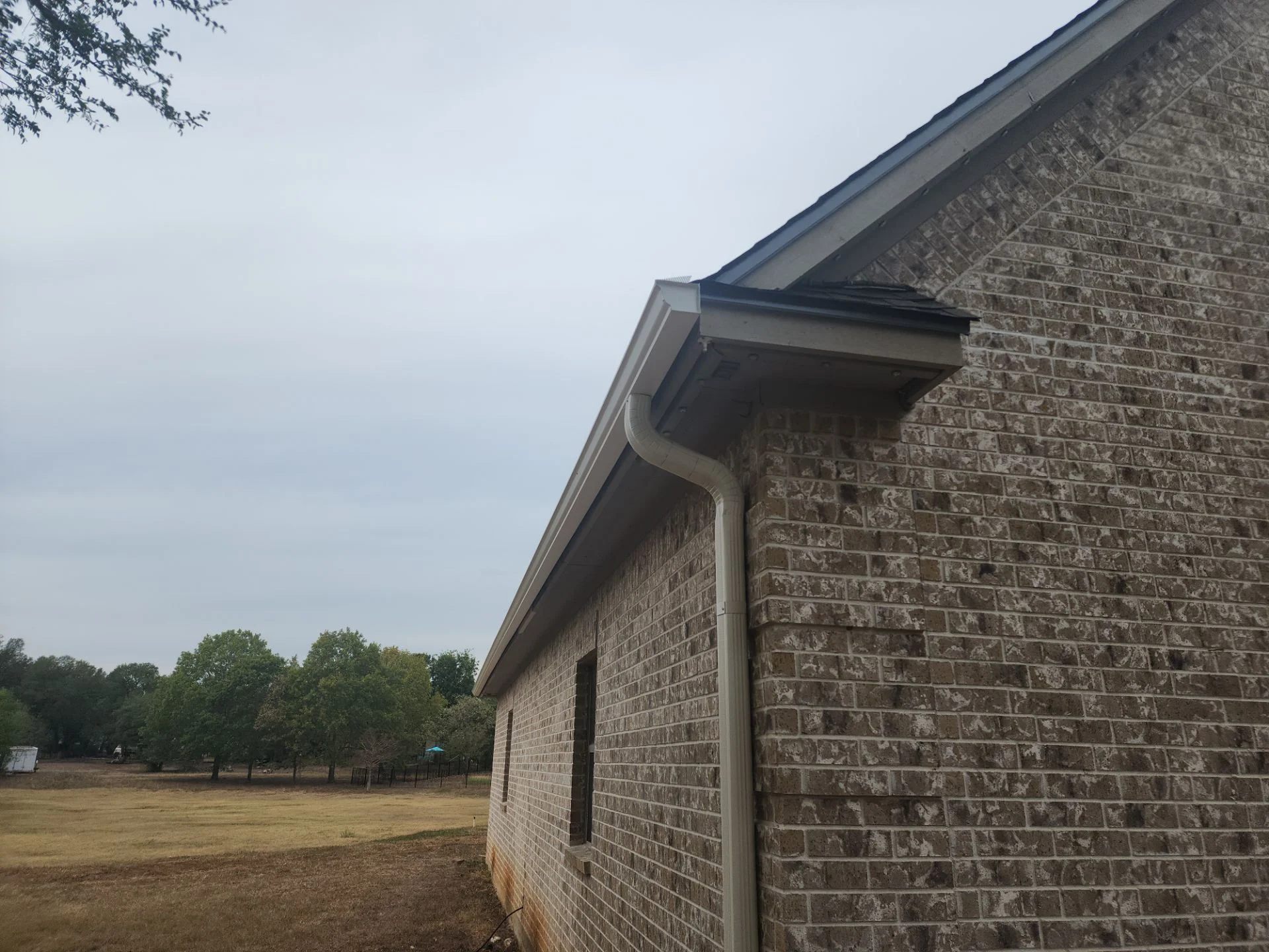 Gutter and downspout at the roof edge, Austin TX - Driftwood Builders Roofing - Driftwood Builders Roofing Gutter and downspout running along the roof edge of a brick home on a Driftwood Builders Roofing project in the Austin, TX area