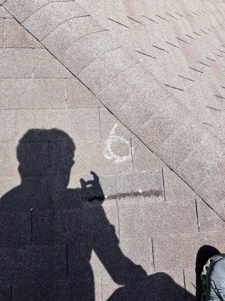 Roof inspector marking a hail strike in chalk on an asphalt shingle roof in Austin, TX