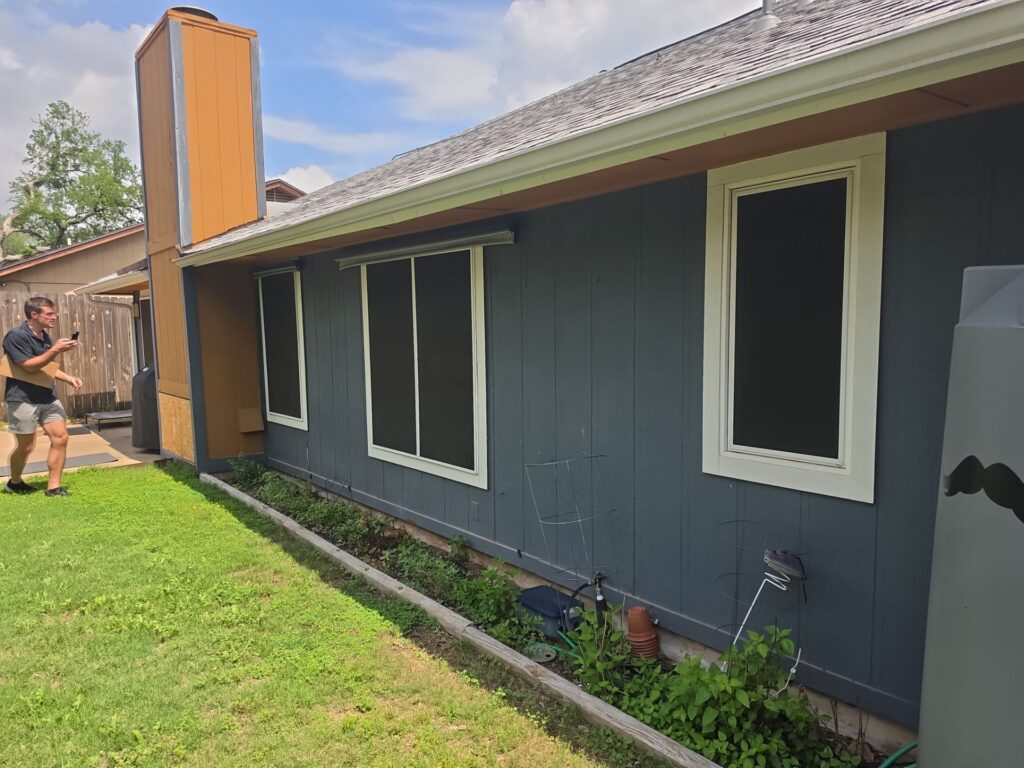 Estimator photographing the existing vertical panel siding and window trim on an Austin home before pricing the project.