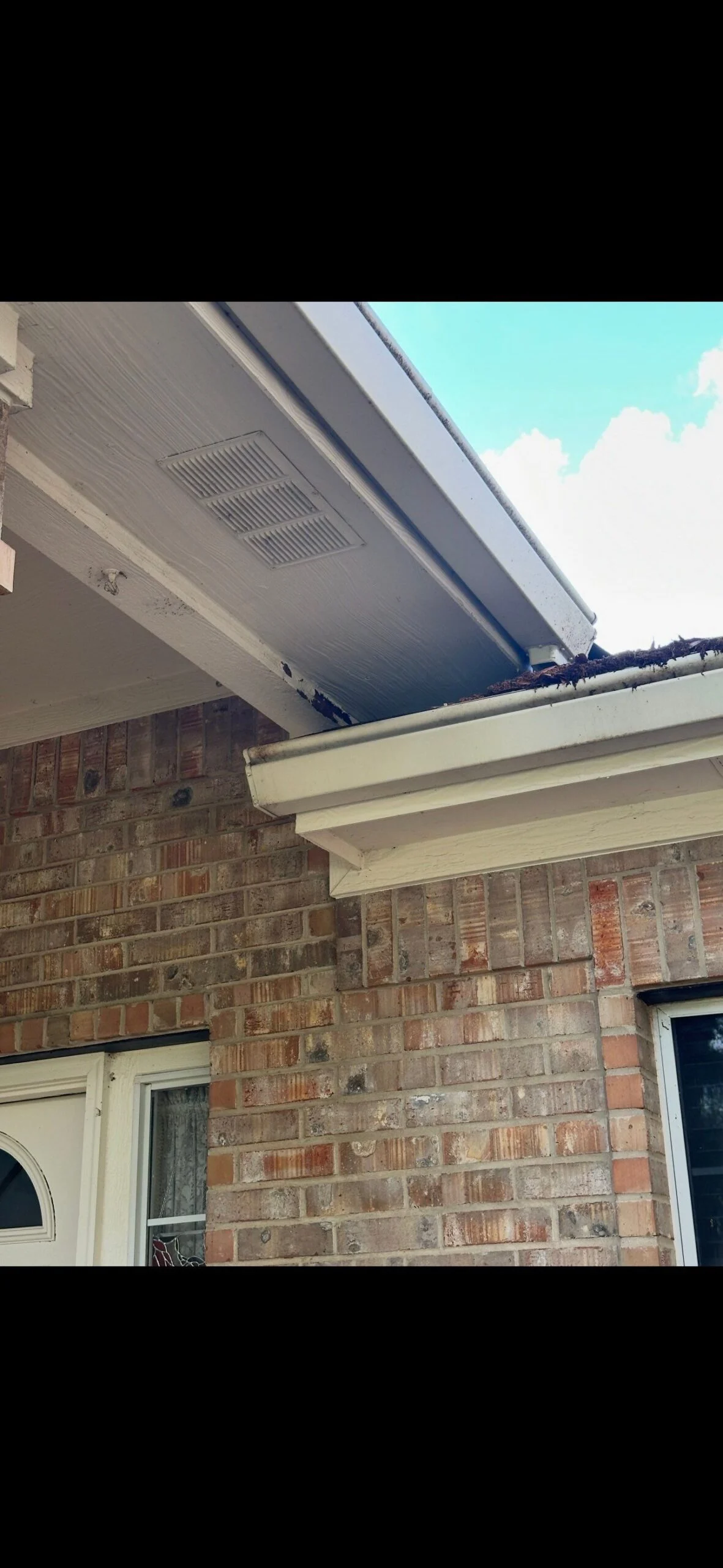 A gutter and fascia corner showing dark water staining on the fascia board and debris buildup where the gutter meets the roofline, on a real Driftwood siding repair project in Austin